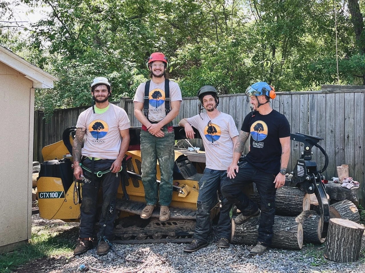 Four tree service professionals posing with equipment in nature.